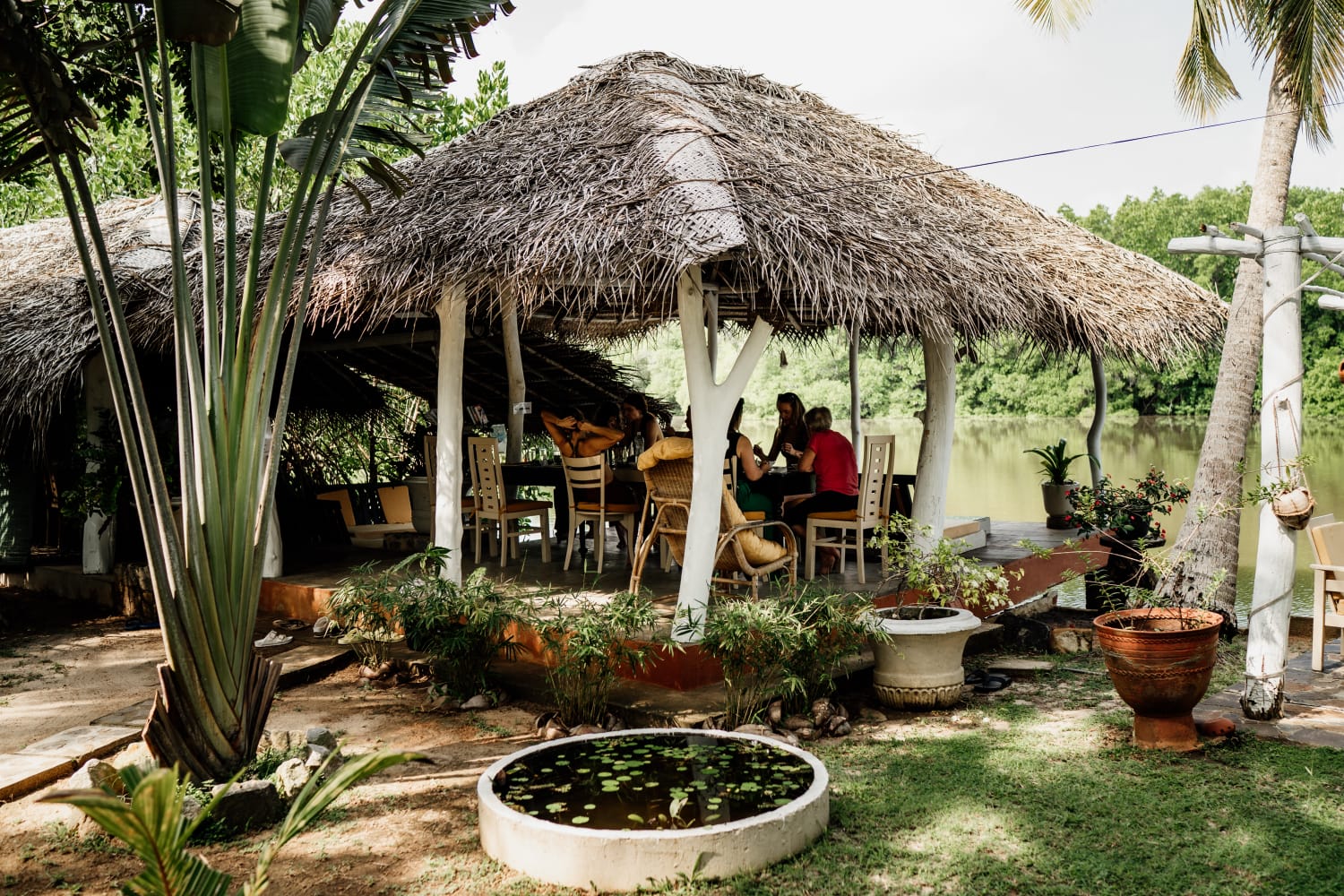 Guests sharing a meal under the open thatched pavilion beside the lagoon