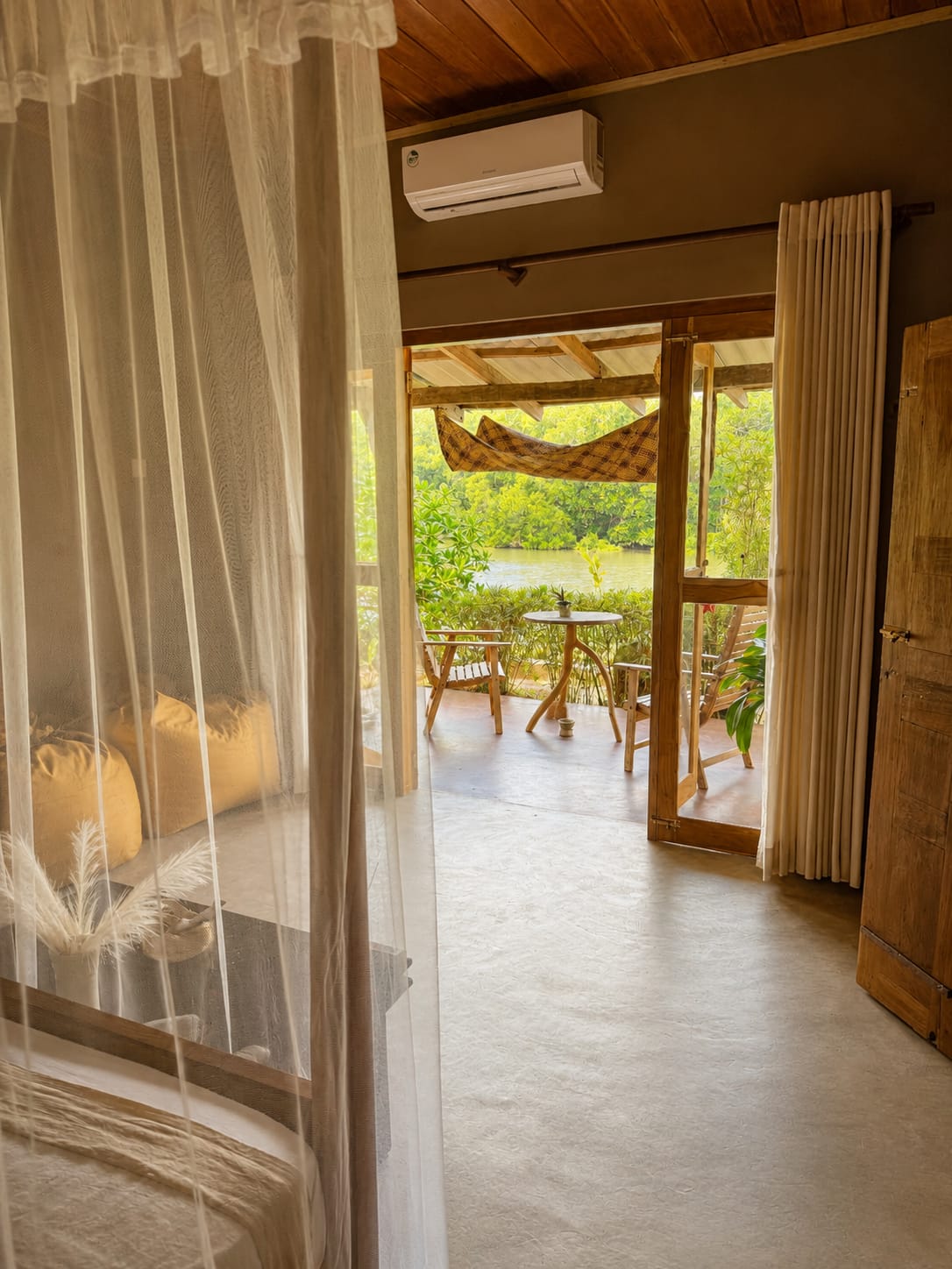 Bedroom with mosquito net opening onto a private terrace with hammock and lagoon view
