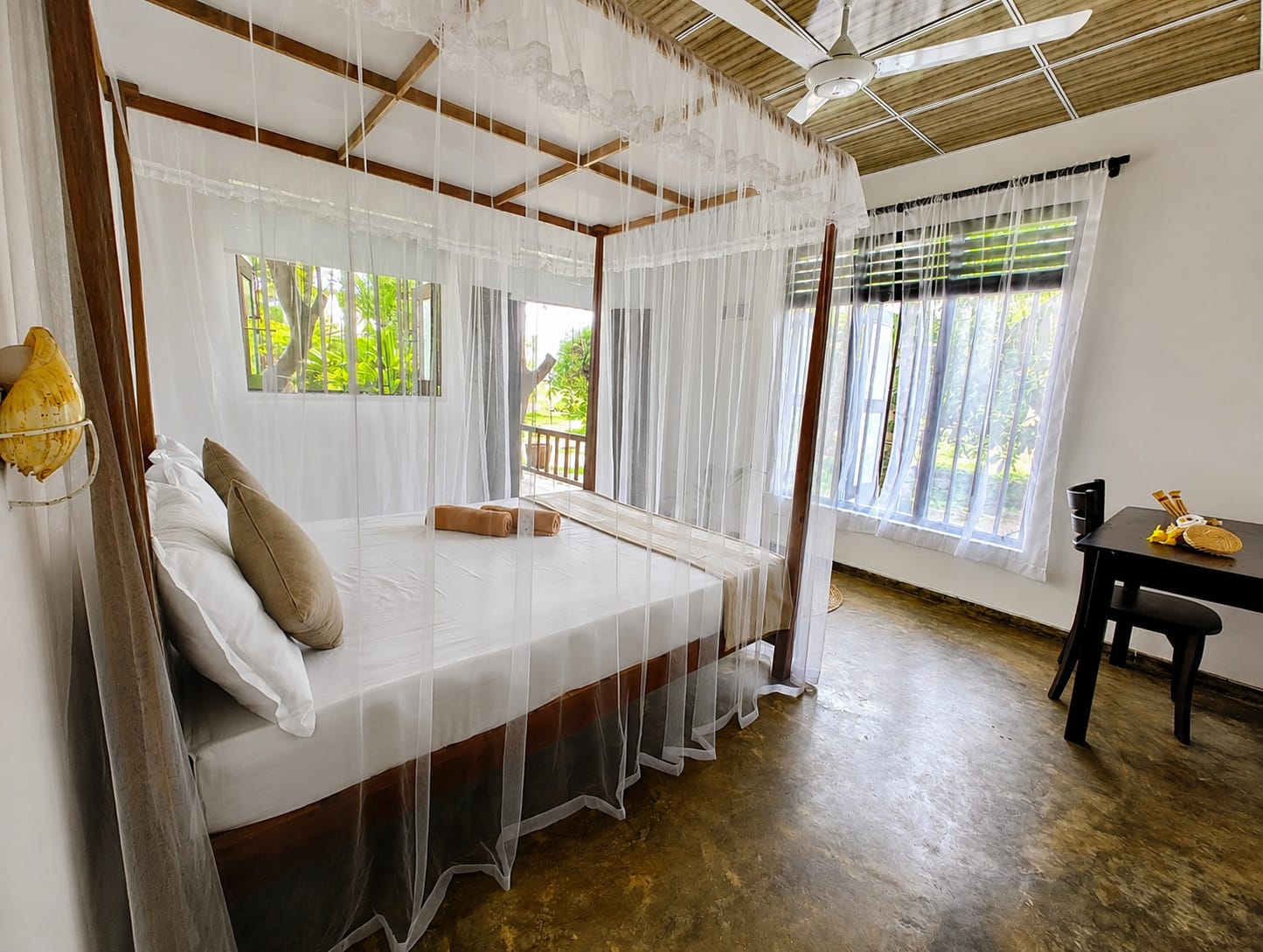 Bright bungalow bedroom with a four-poster bed, mosquito net and garden views